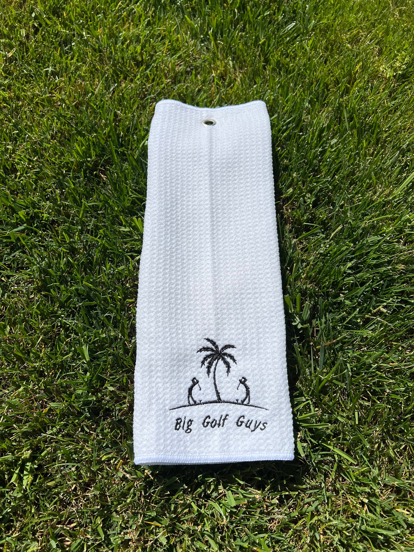 gray waffle towel with black big golf guys logo grass background