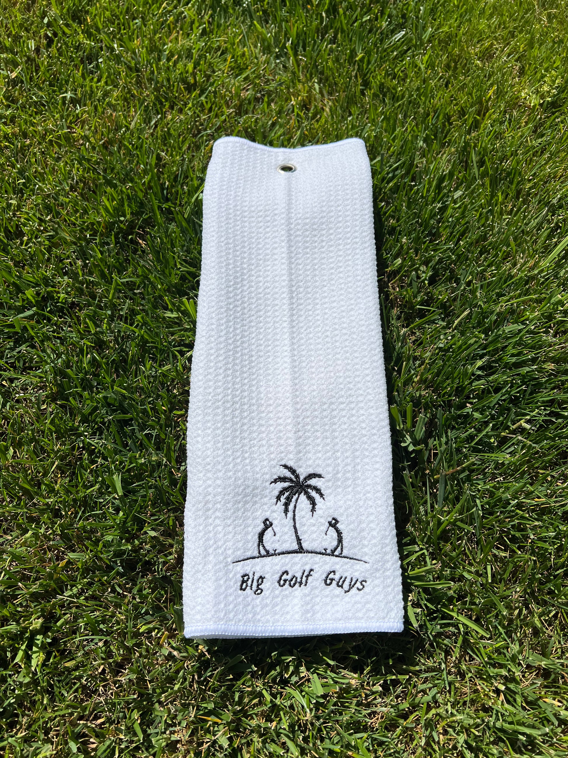gray waffle towel with black big golf guys logo grass background