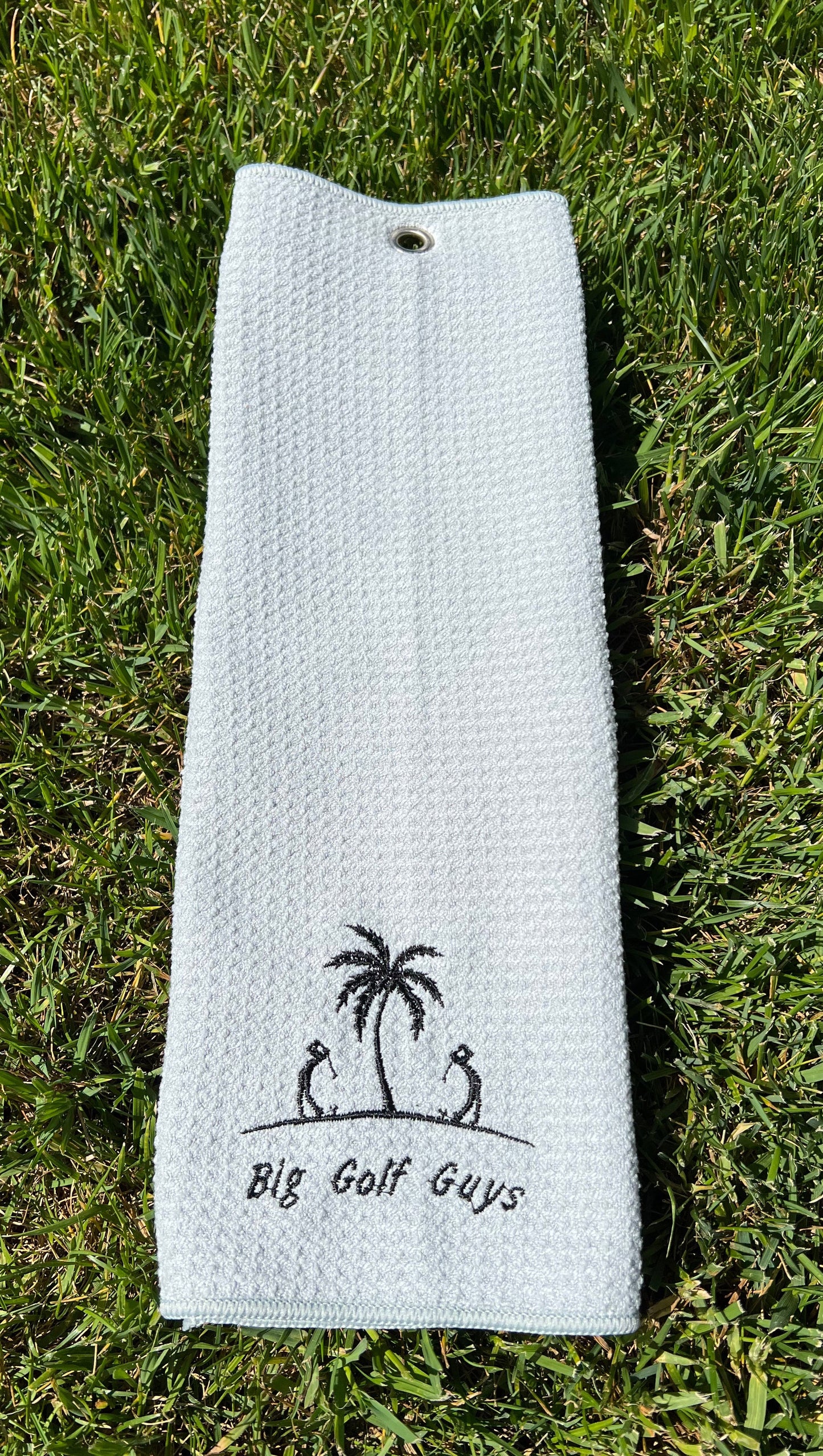 gray waffle towel with black big golf guys logo with grass background